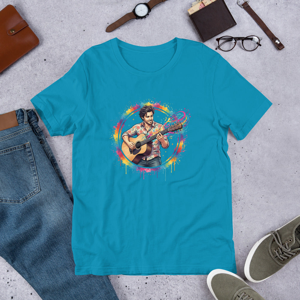 Blue t-shirt with a colorful graphic of a person playing guitar, surrounded by jeans, shoes, and accessories on a concrete surface.