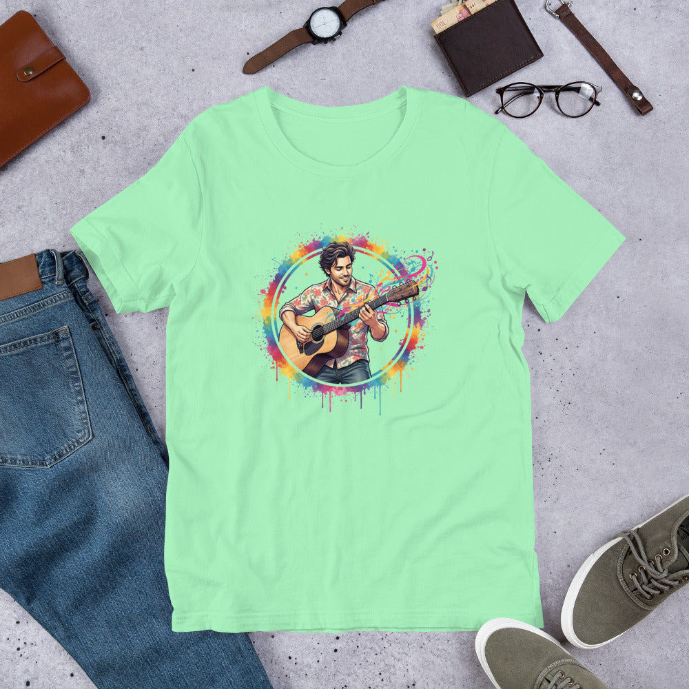 Light green t-shirt with a colorful graphic of a person playing guitar, placed on a concrete surface with jeans, shoes, and accessories.
