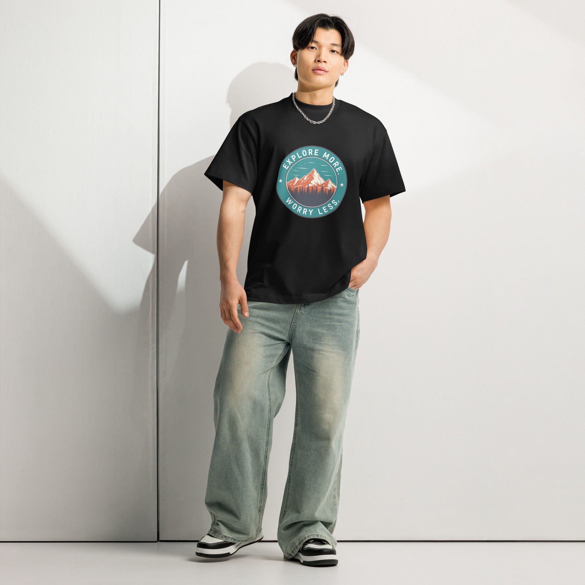 Person wearing a black t-shirt with a mountain graphic and text against a white wall.
